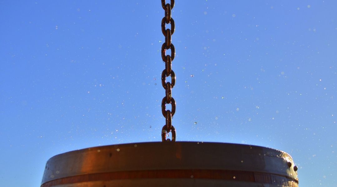 A rain chain directing rain towards a barrel below it.